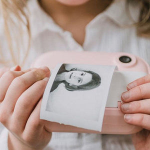 child holding pink instant print camera printing black and white photo of woman face