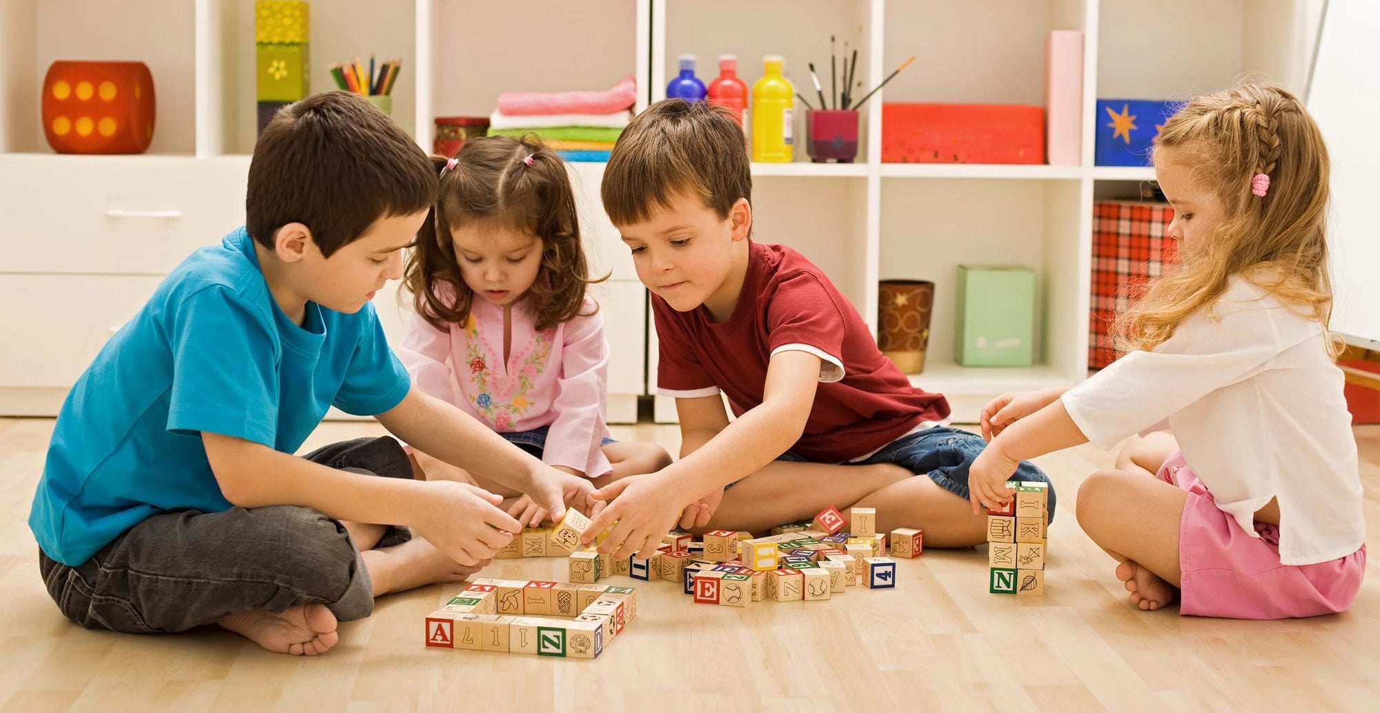 Children playing together with educational wooden blocks on the floor in a bright, organized playroom.