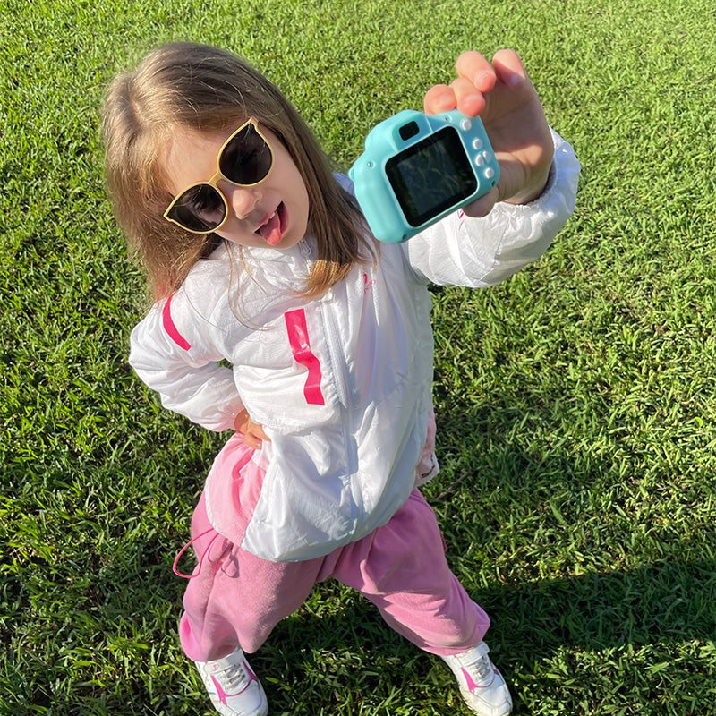 Child outdoors holding a blue LittleLens Kids Camera with sunglasses on bright sunny day