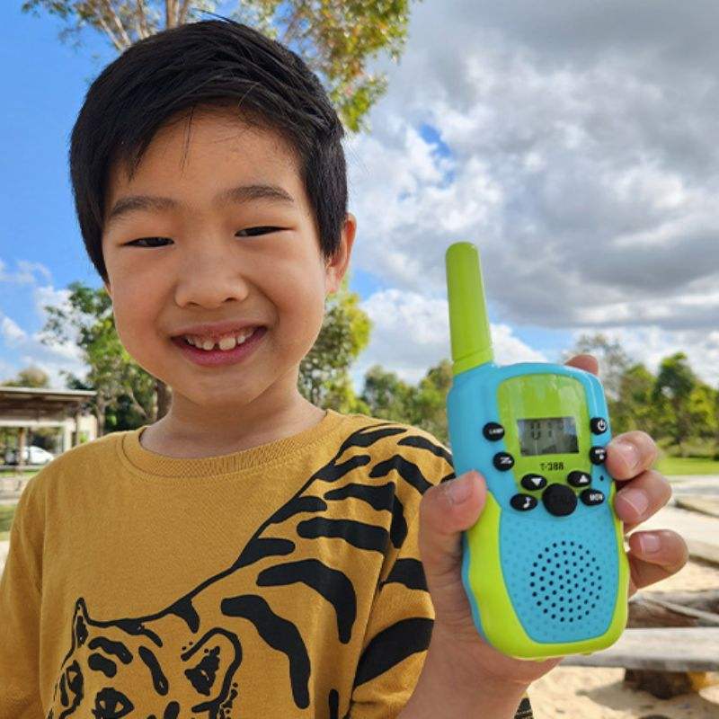 child holding blue and green kids walkie talkie outdoors with smiling face and cloudy sky background